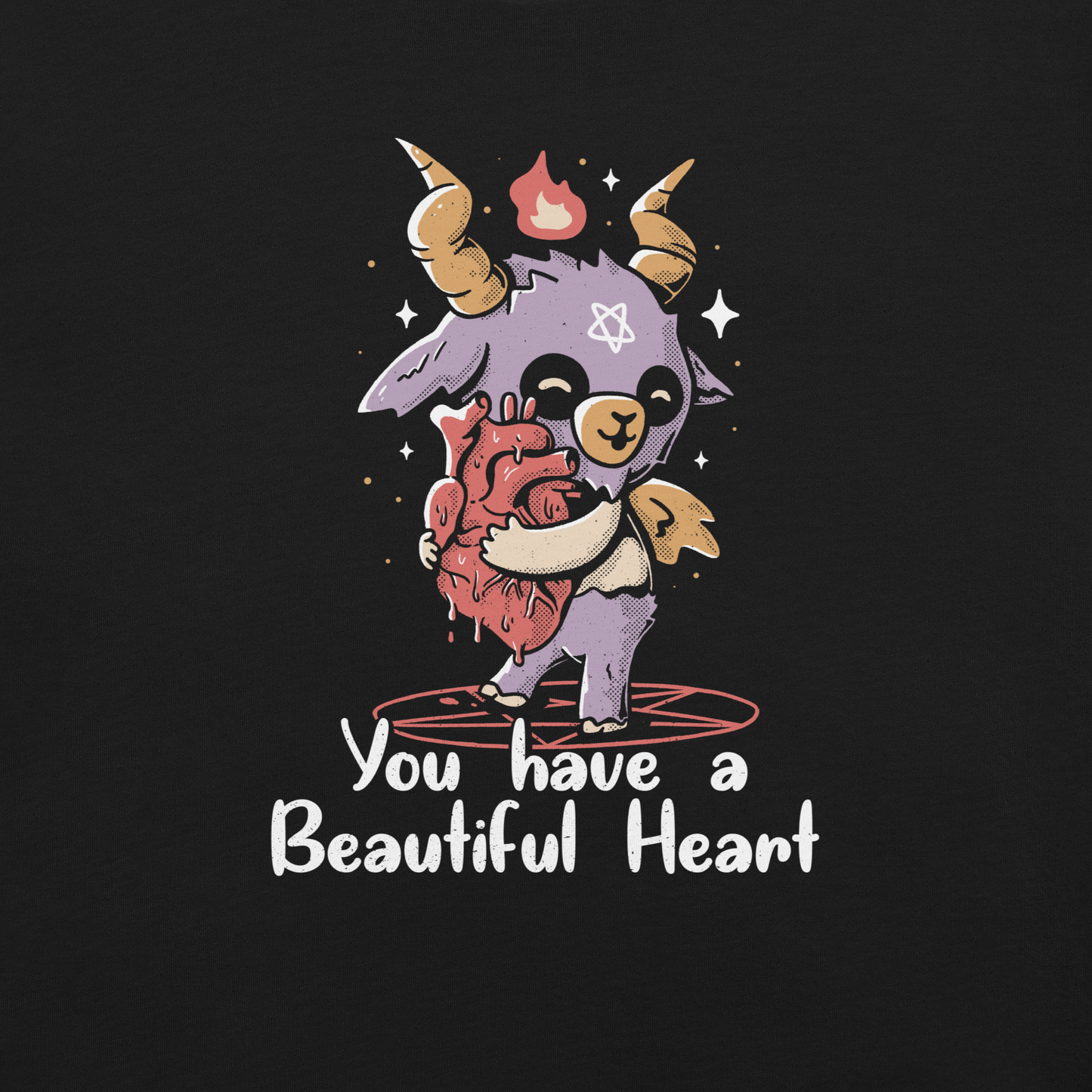 The design features a cute, cartoonish, anthropomorphic goat with big horns and a flame above its head, standing on a red pentagram. The goat has a star on its forehead and is hugging a large, anatomically correct human heart. The text below reads, 'You have a Beautiful Heart'. The image combines elements of occult symbolism with a playful, endearing aesthetic.