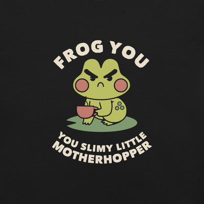 The design features a cartoonish green frog with exaggerated angry features, holding a teacup. The frog has round red cheeks. Above it, text says 'Frog You' and below, 'You Slimy Little Motherhopper'. The style is playful and humorous, reminiscent of cute comic art.