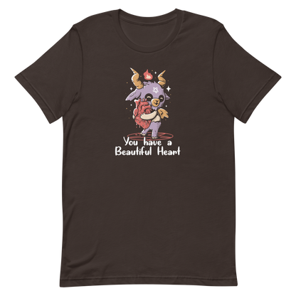 The design features a cute, cartoonish, anthropomorphic goat with big horns and a flame above its head, standing on a red pentagram. The goat has a star on its forehead and is hugging a large, anatomically correct human heart. The text below reads, 'You have a Beautiful Heart'. The image combines elements of occult symbolism with a playful, endearing aesthetic.