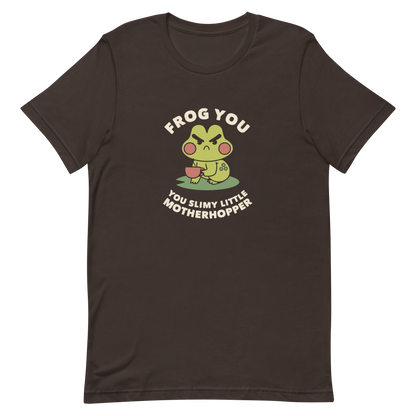 The design features a cartoonish green frog with exaggerated angry features, holding a teacup. The frog has round red cheeks. Above it, text says 'Frog You' and below, 'You Slimy Little Motherhopper'. The style is playful and humorous, reminiscent of cute comic art.