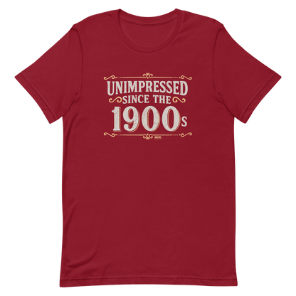 Vintage-style graphic with the phrase “Unimpressed Since the 1900s” in bold distressed lettering, decorated with ornate flourishes and a retro color palette.