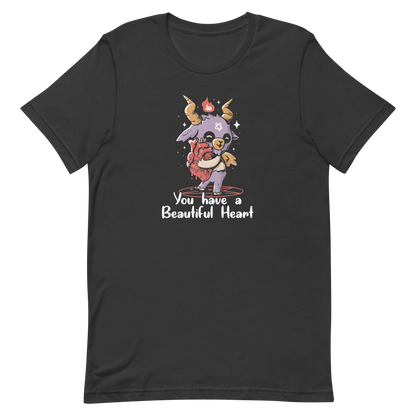The design features a cute, cartoonish, anthropomorphic goat with big horns and a flame above its head, standing on a red pentagram. The goat has a star on its forehead and is hugging a large, anatomically correct human heart. The text below reads, 'You have a Beautiful Heart'. The image combines elements of occult symbolism with a playful, endearing aesthetic.