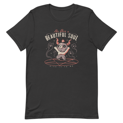 This design features a cute, cartoonish character with horns and a pentagram on its forehead, standing on a red circle with ghost-like figures surrounding it. Above the character, the text reads 'You have a beautiful soul,' and below, 'Give it to me.' The design contrasts dark and cute imagery with playful lettering.