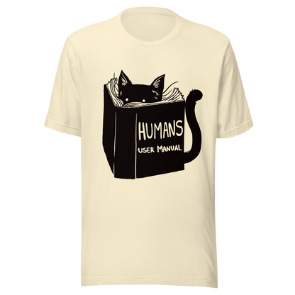 A kitten peeking out from behind a huge book titled "Humans: User Manual". This design plays on the idea that cats are trying to figure out how to control us. Perfect for cat lovers, book fans, and anyone who enjoys lighthearted humor in prints.