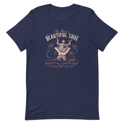 This design features a cute, cartoonish character with horns and a pentagram on its forehead, standing on a red circle with ghost-like figures surrounding it. Above the character, the text reads 'You have a beautiful soul,' and below, 'Give it to me.' The design contrasts dark and cute imagery with playful lettering.
