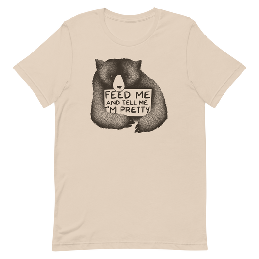 This drawing is of a cute, cartoon-style bear holding a sign with a heart-shaped nose and simple, expressive eyes. The sign reads, 'Feed me and tell me I'm pretty' in a handwritten, playful font. The bear's fur is detailed with fine, textured lines, giving it a cozy, endearing look. The drawing has a monochrome, black-and-white color scheme