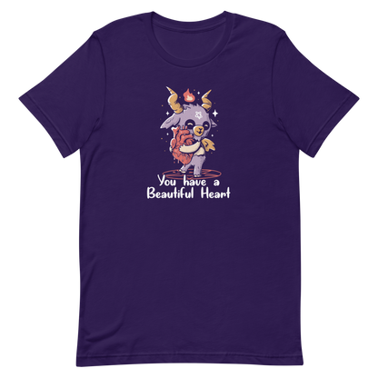 The design features a cute, cartoonish, anthropomorphic goat with big horns and a flame above its head, standing on a red pentagram. The goat has a star on its forehead and is hugging a large, anatomically correct human heart. The text below reads, 'You have a Beautiful Heart'. The image combines elements of occult symbolism with a playful, endearing aesthetic.