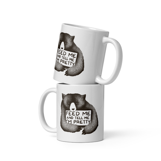 This drawing is of a cute, cartoon-style bear holding a sign with a heart-shaped nose and simple, expressive eyes. The sign reads, 'Feed me and tell me I'm pretty' in a handwritten, playful font. The bear's fur is detailed with fine, textured lines, giving it a cozy, endearing look. The drawing has a monochrome, black-and-white color scheme