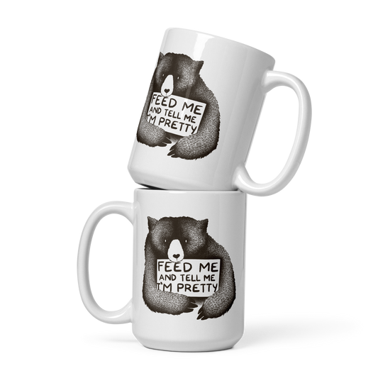 This drawing is of a cute, cartoon-style bear holding a sign with a heart-shaped nose and simple, expressive eyes. The sign reads, 'Feed me and tell me I'm pretty' in a handwritten, playful font. The bear's fur is detailed with fine, textured lines, giving it a cozy, endearing look. The drawing has a monochrome, black-and-white color scheme